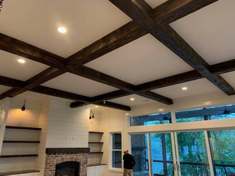 Dark-stained timber beams crossing a white ceiling above a brick fireplace