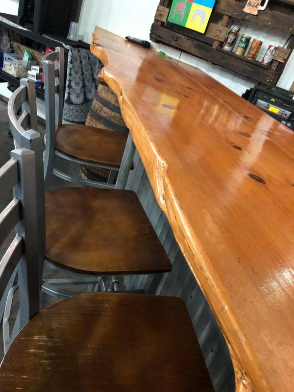A glossy live-edge wood bar top lined with wooden stools. Opens larger.