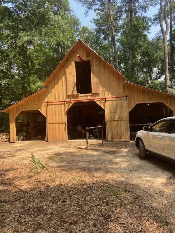 A rough-sawn wood barn with a high loft door and three open bays. Opens larger.