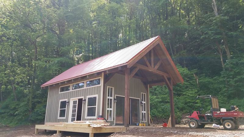 A small gray cabin with a red metal roof and a timber-frame porch gable