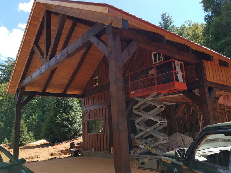 A timber-frame porch with heavy dark posts and curved braces on a board-and-batten building. Opens larger.