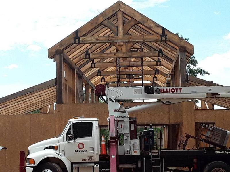 A crane truck lifting timber trusses into place on a building frame. Opens larger.