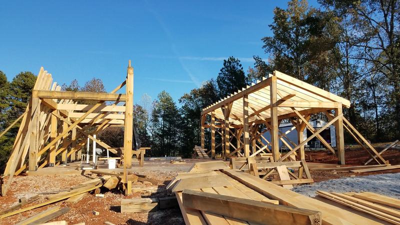 Two timber frames going up side by side on a cleared site. Opens larger.
